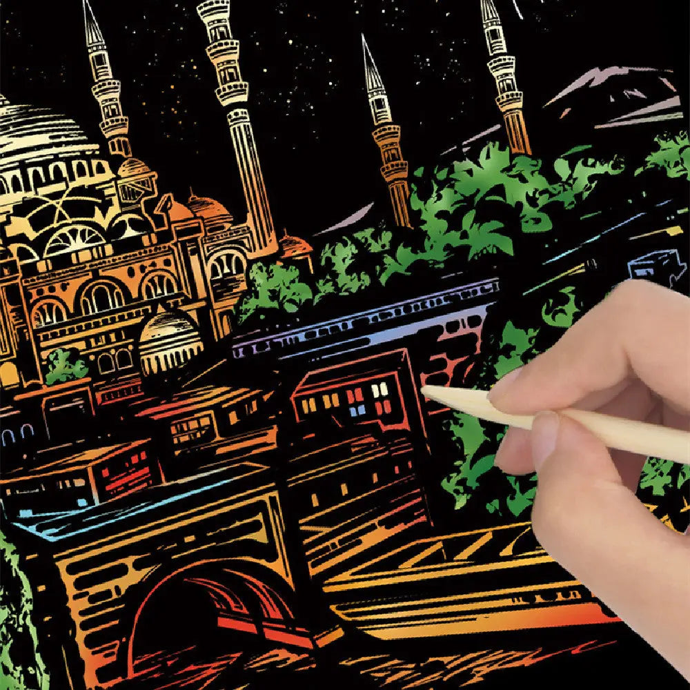 Hand holding a stylus over a Scratch Art cityscape with illuminated buildings.